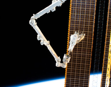 Astronaut Woody Hoburg carries a rolled-up solar array while riding the Canadarm2 robotic arm outside the International Space Station