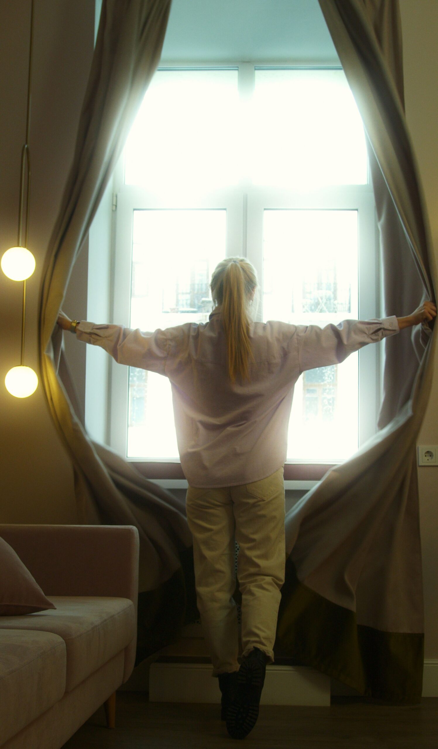 A person opening curtains to let morning light into a bedroom