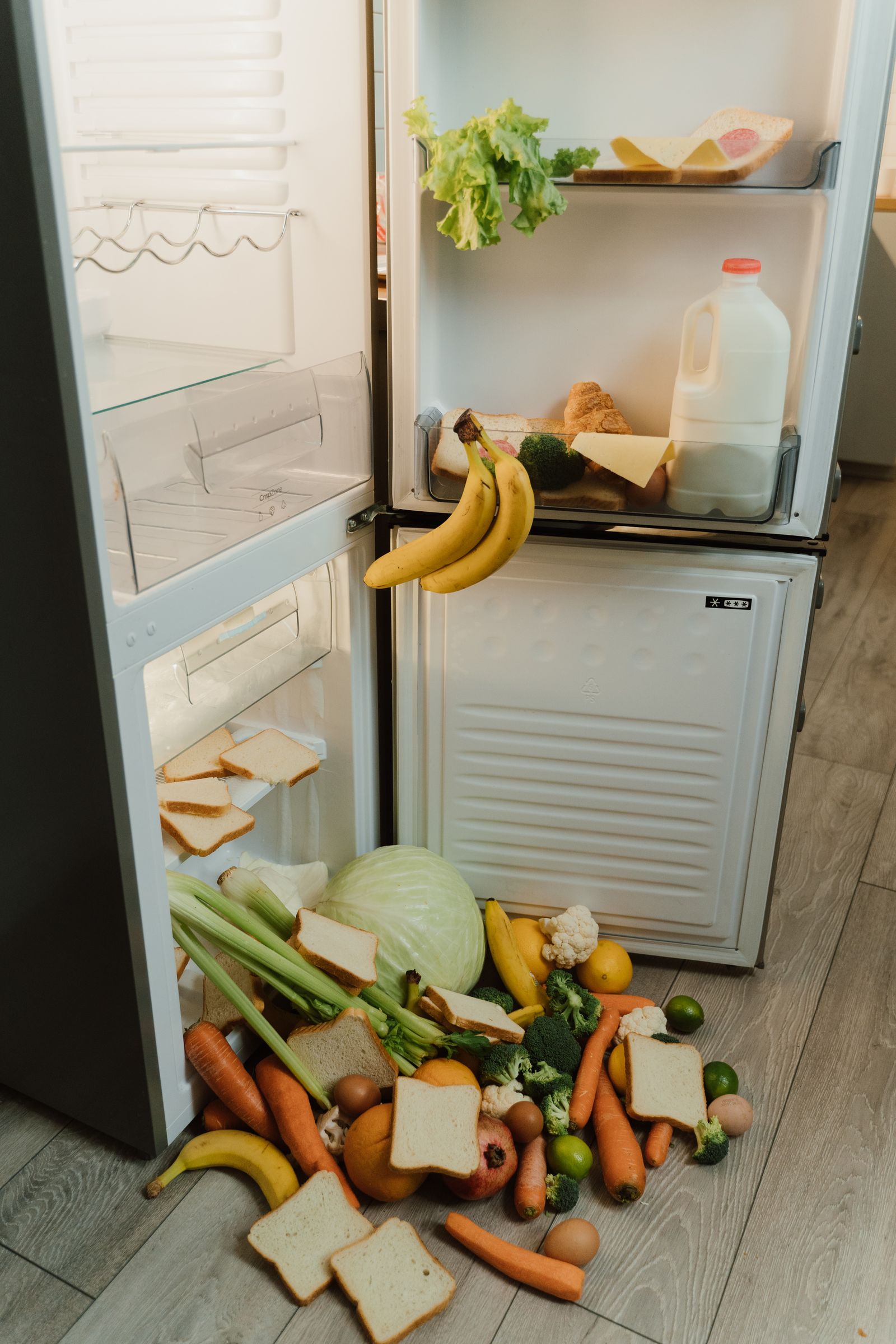 Open refrigerator with bread and vegetables placed on the floor