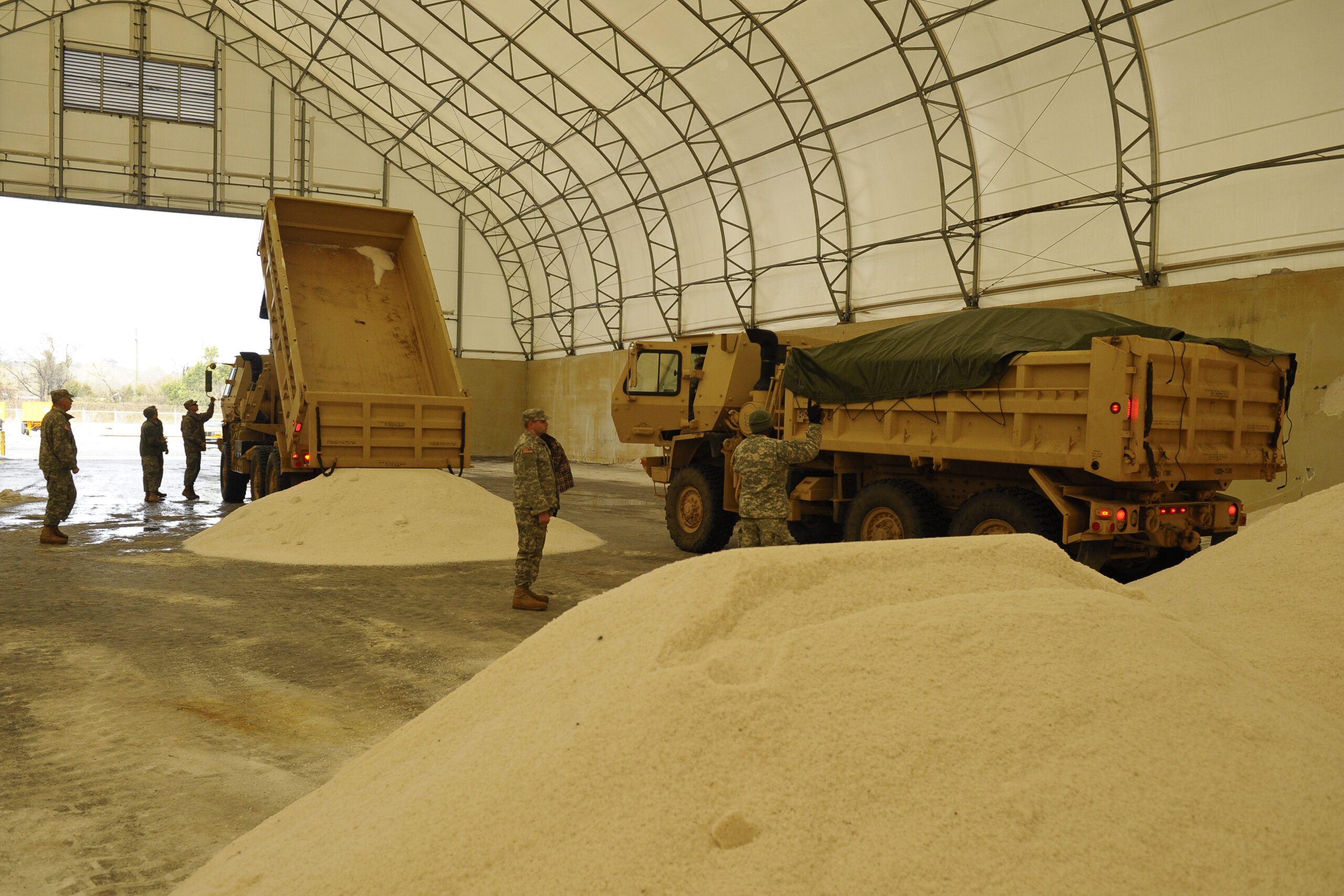 A large pile of road salt beside dump trucks prepared for winter road maintenance