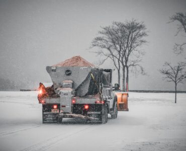 A road maintenance truck spreads salt on a snow-covered road during a winter storm
