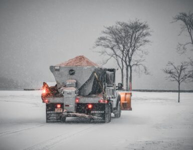 A road maintenance truck spreads salt on a snow-covered road during a winter storm