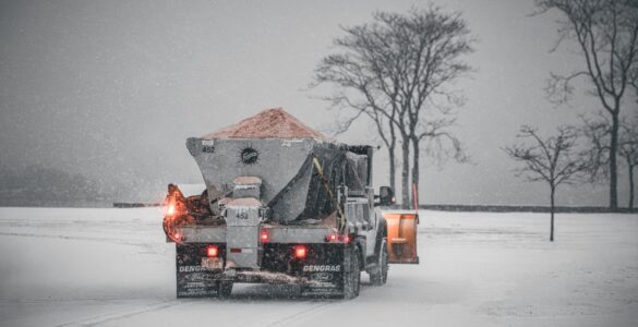 A road maintenance truck spreads salt on a snow-covered road during a winter storm