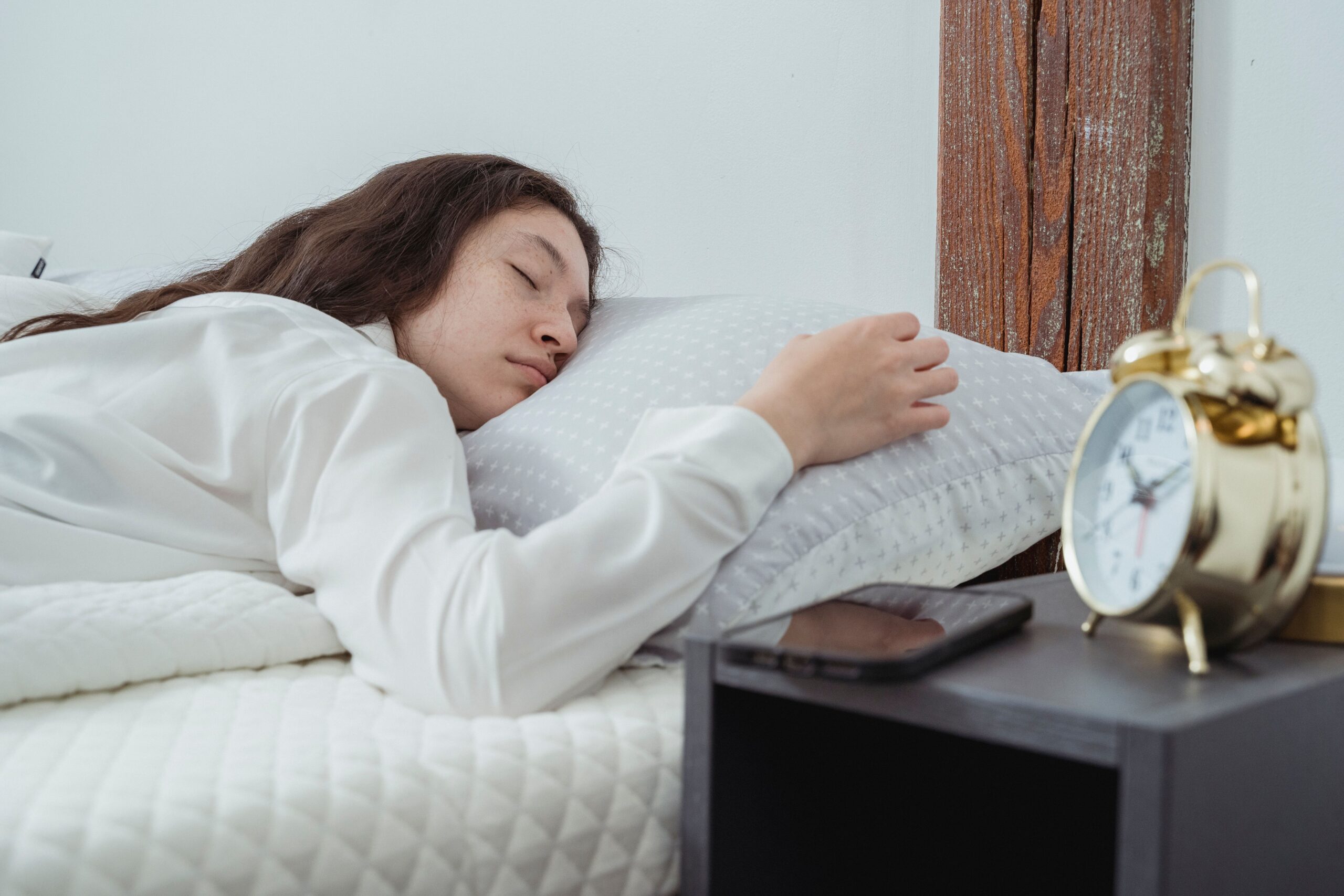 A person sleeping beside an alarm clock and smartphone