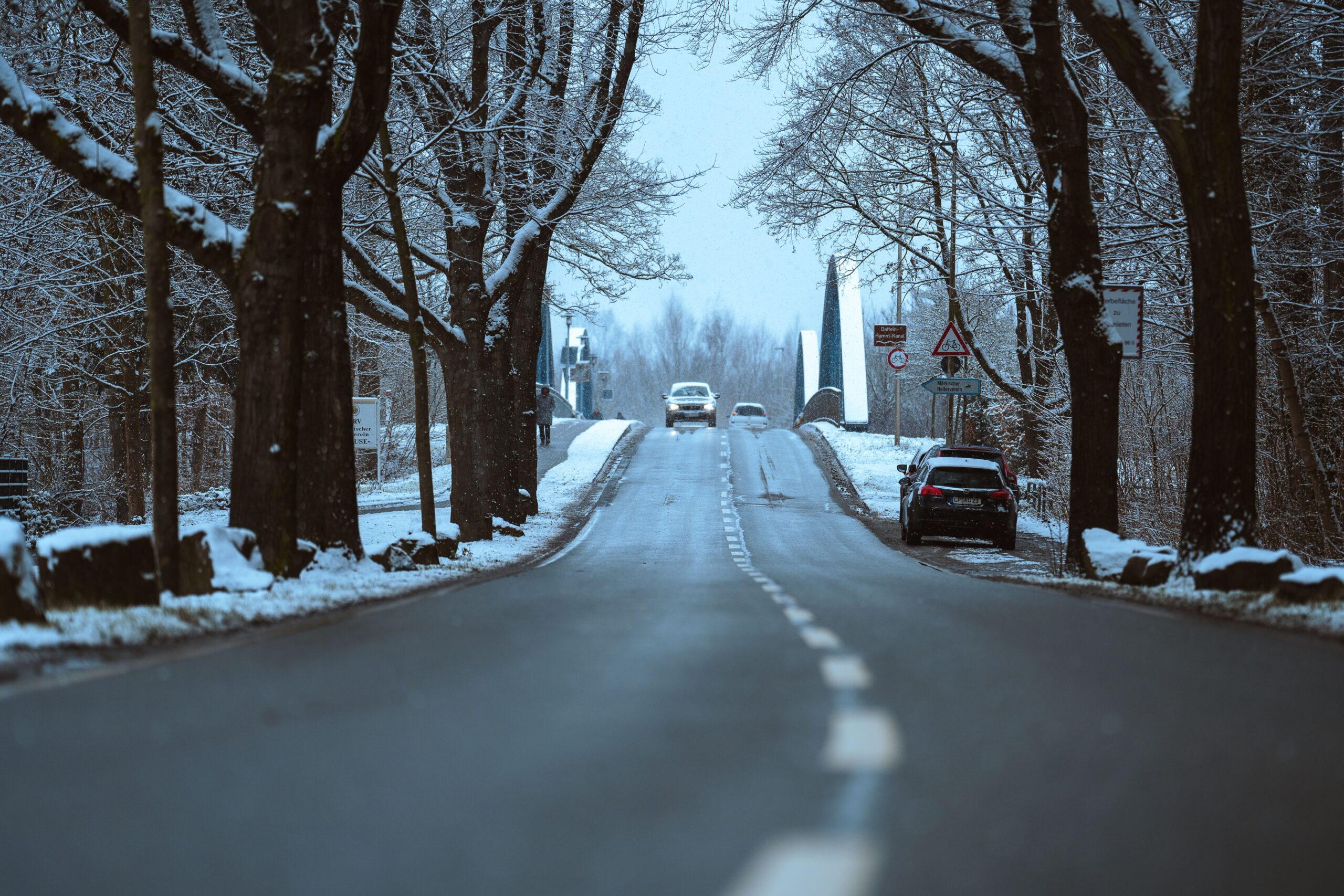 Cars with headlights on along a snow-lined winter road