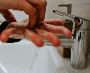 Hands covered in soap lather being washed under running water