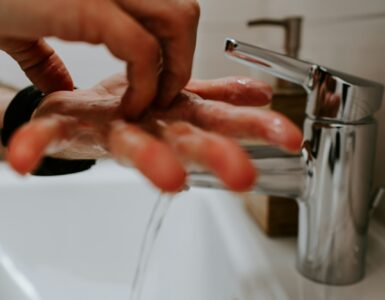 Hands covered in soap lather being washed under running water