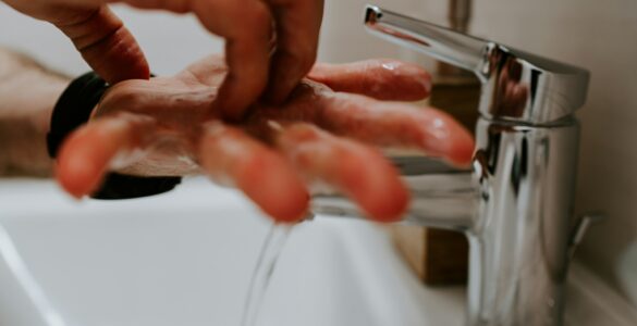 Hands covered in soap lather being washed under running water