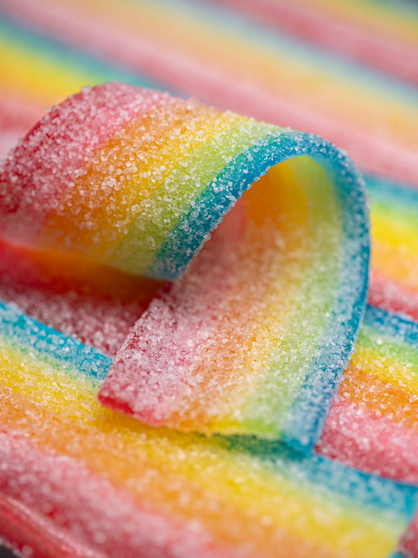 Close-up of a rainbow sour candy strip coated in sugar crystals