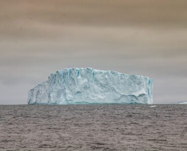 Large iceberg rising from dark Antarctic waters beneath a cloudy sky