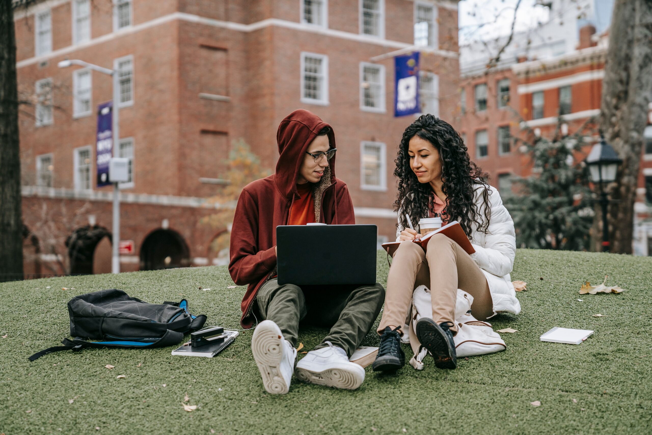 Two college students reviewing information on a laptop and notebook