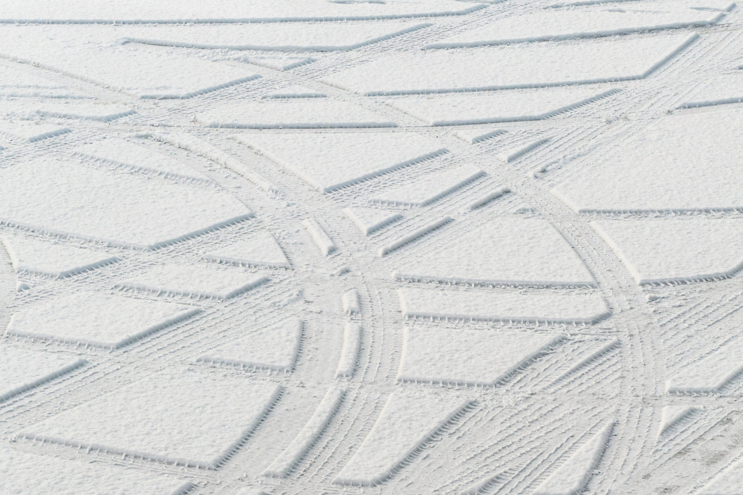 Curving car tire tracks across fresh snow in a parking area