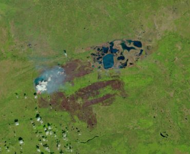 Satellite view of wildfire smoke spreading over a green landscape in western Canada
